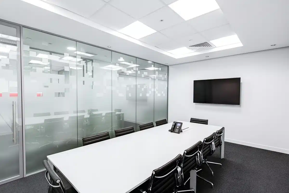 A wide, empty modern boardroom table with folded meeting folders and a generic tablet at one place; late-morning light through blinds suggests a corporate announcement setting