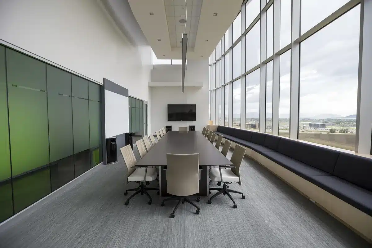 An empty oval conference table with a single microphone at the head, papers scattered, an open notebook and a pen left on the table — atmosphere of a geopolitics briefing room