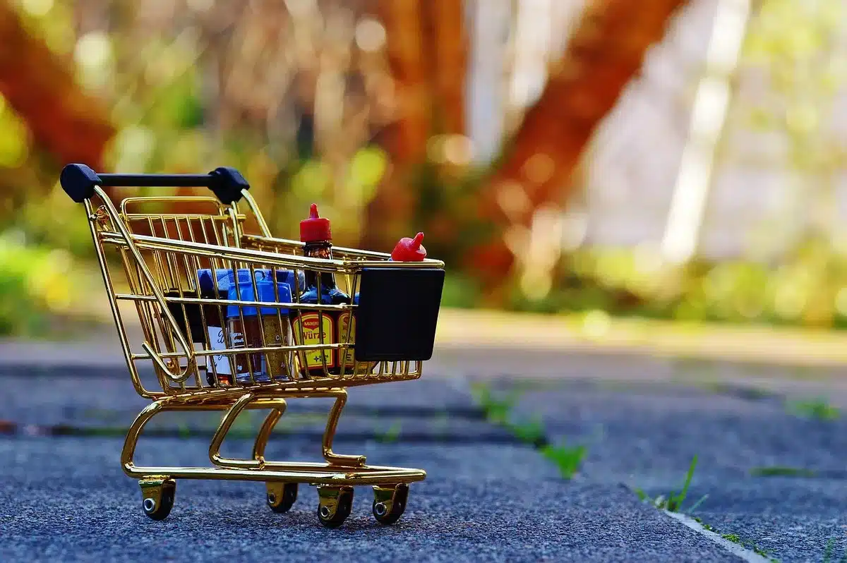 Anonymous close-up of a shopping cart filled with bulk-packaged goods, blurred warehouse racks in background, no logos visible
