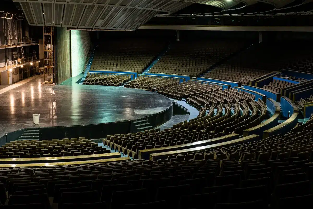 Empty conference stage with a single microphone on a small table, a closed curtain behind it, subtle spot lighting on the mic, no logos or text