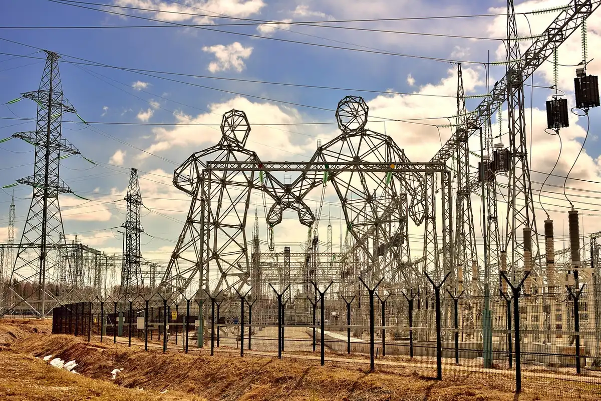 A pair of anonymous technicians near a fenced electrical substation at a remote site, silhouetted against utility towers and transformers, no identifying marks