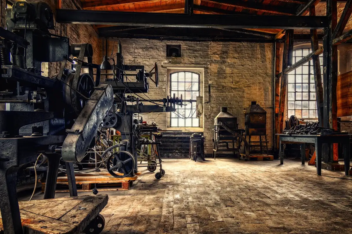 A dim factory production line with anonymous workers' tools and empty workstations under overhead lights, a single industrial door ajar suggesting recent entry