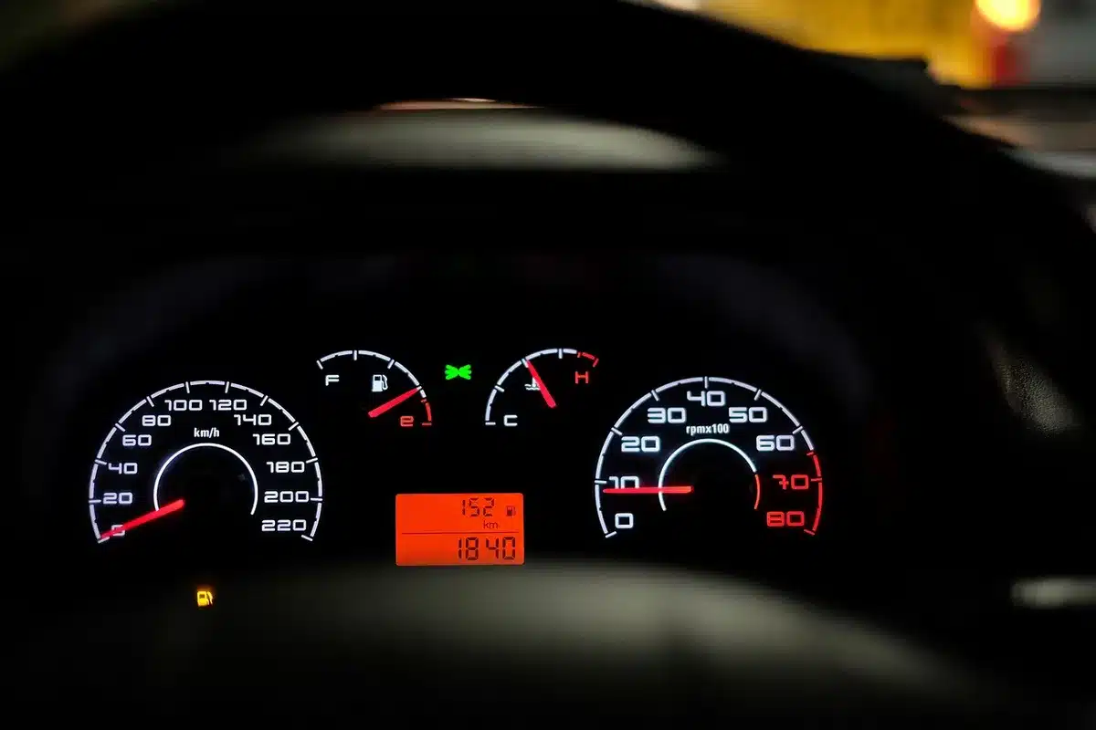 Close-up of an unbranded fuel gauge and a gloved hand on a clipboard beside a pallet of cargo, anonymous and logo-free