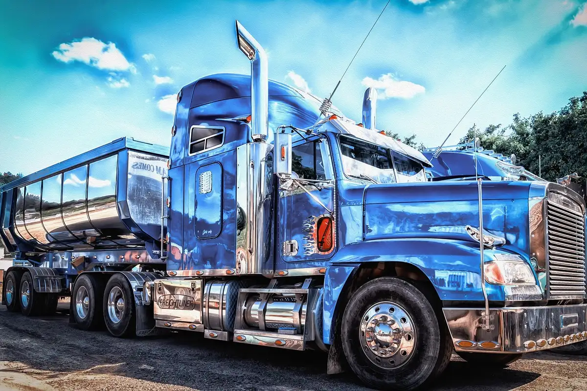 Anonymous long-haul trucks parked at a dimly lit depot, drivers silhouetted, pallets stacked nearby suggesting shipping pressure