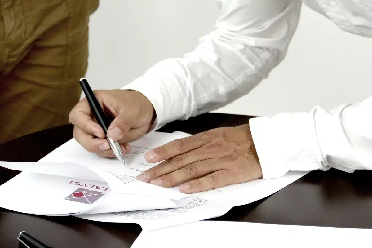 A stack of documents and folders on a desk with a magnifying glass and pen, suggesting investigation and document review