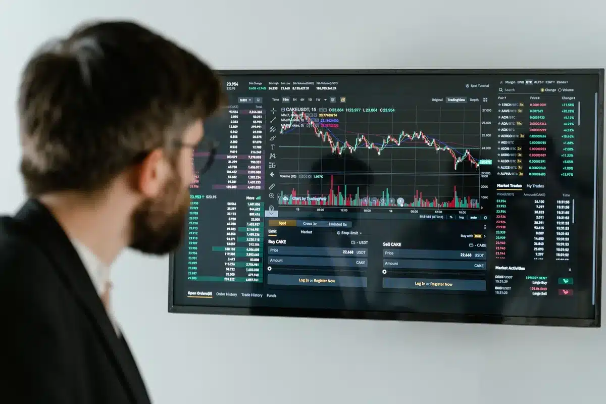 Anonymous investor silhouette looking at multiple ticker screens, back to camera, dim trading-room interior