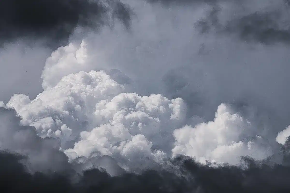 Storm clouds darkening over residential neighborhoods with power lines visible against the sky, severe weather approaching, tension and anticipation