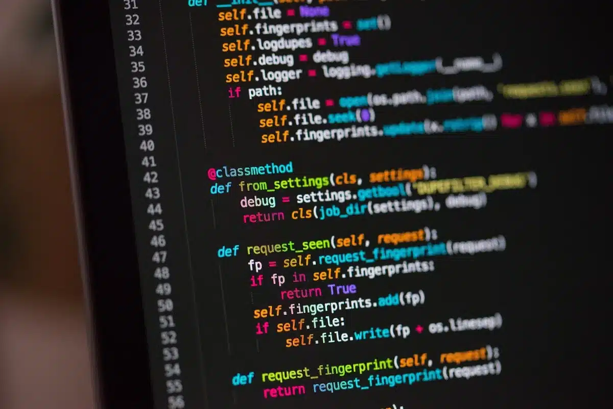 Anonymous hands on a laptop keyboard in a dark room, a line of red and blue code reflected on the screen, no logos or identifiable devices — tension