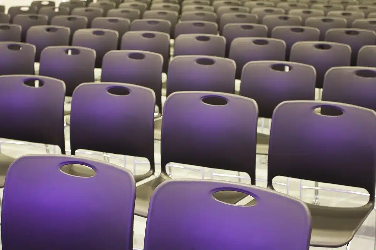 A sleek conference hall interior with empty chairs arranged in rows, morning light streaming through tall windows, a podium awaiting speakers, subtle French architectural details visible in the background, conveying anticipation and absence.