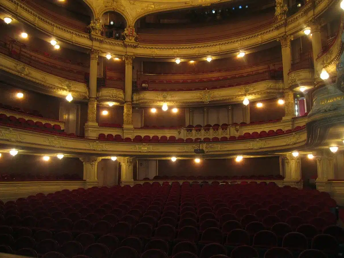 Empty auditorium with a single microphone on the stage under a spotlight, dust motes visible in the beam; no people, no logos