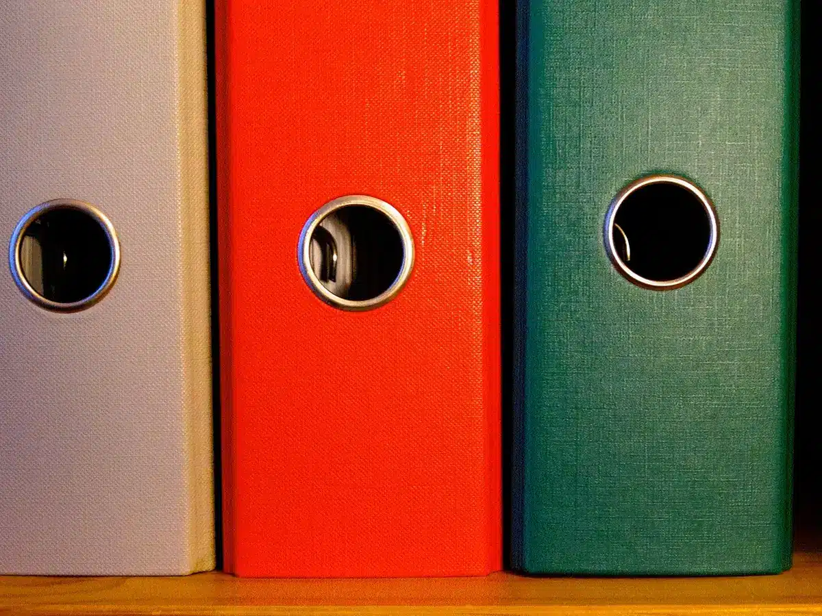 A stack of sealed manila file folders bound with red tape, one folder slightly open revealing typed pages beneath, soft overhead lighting