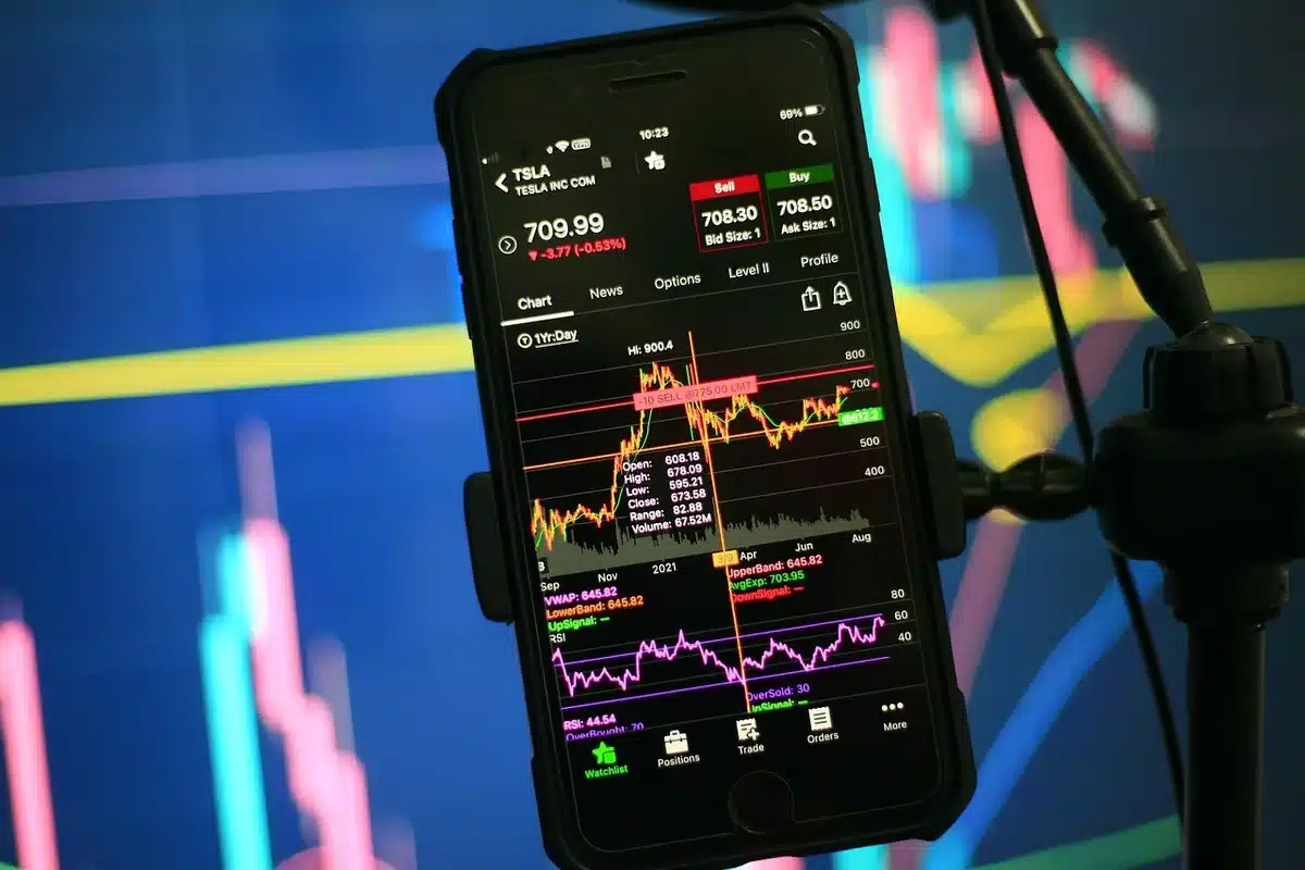 A stock market trading floor with multiple screens displaying red downward arrows and declining price charts, traders monitoring positions intently, warm overhead lighting casting shadows across the desk.