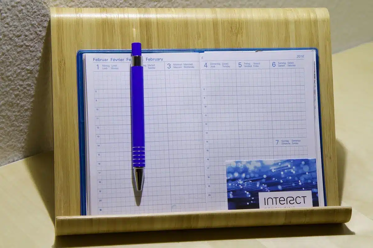 An empty trader workstation with three dark monitors showing blurred calendar grids and time columns, a coffee mug at the side and a notepad with handwritten times &mdash; evokes scheduling and preparation
