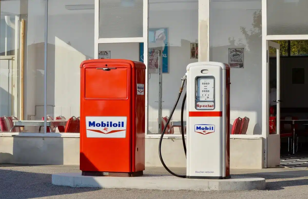 A gas pump display showing $4.14 per gallon in bright red numbers, with blurred cars and a convenience store in the background