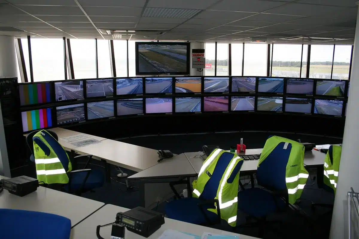 Close-up of an anonymous pair of hands at a keyboard in a control room, a large monitor showing blurred graphs and test names, the scene anonymous and unbranded
