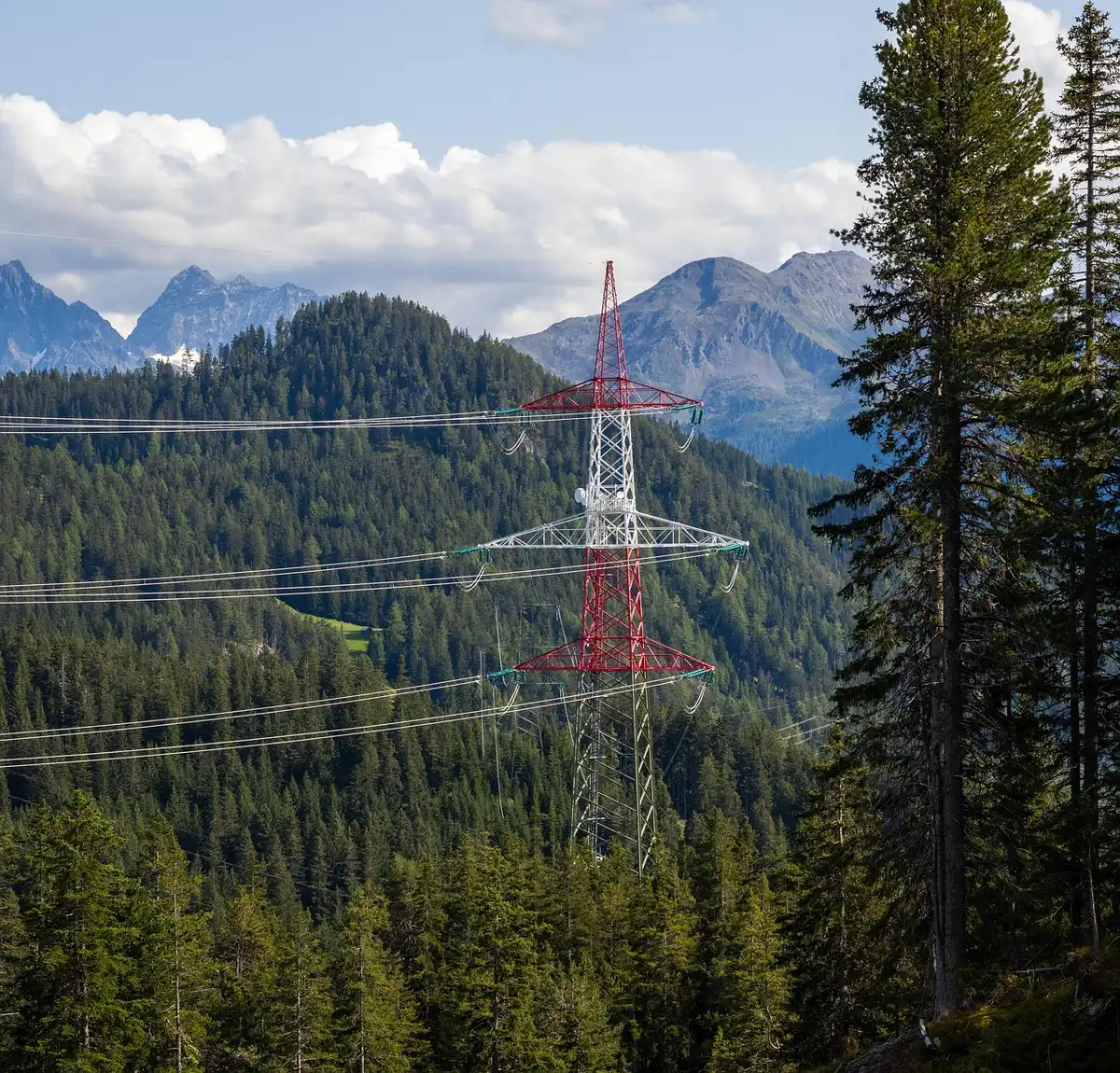 A power transmission tower silhouetted against a dark sky with faint green aurora glow on the horizon, representing the intersection of infrastructure and space weather