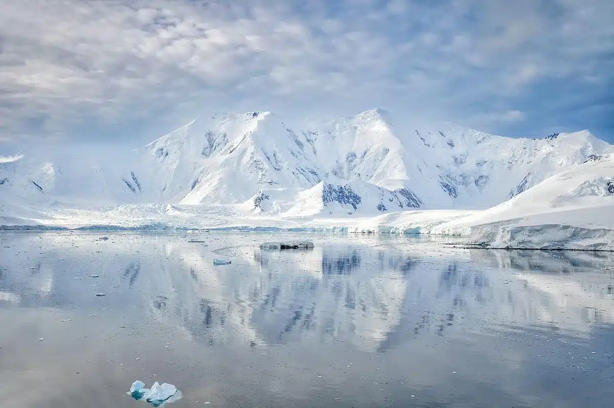 Empty Arctic research station under low sun, distant anonymous equipment and a flagpole without any flag, snow-packed pathway leading toward the building