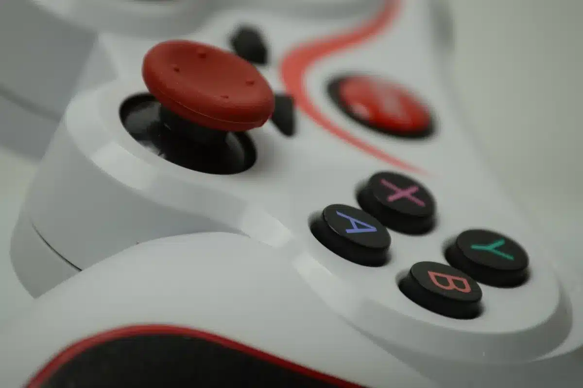 Two limited-edition DualSense controllers in black and white, sitting on a reflective surface with neon pink and blue lighting casting Vice City-inspired shadows and highlights.