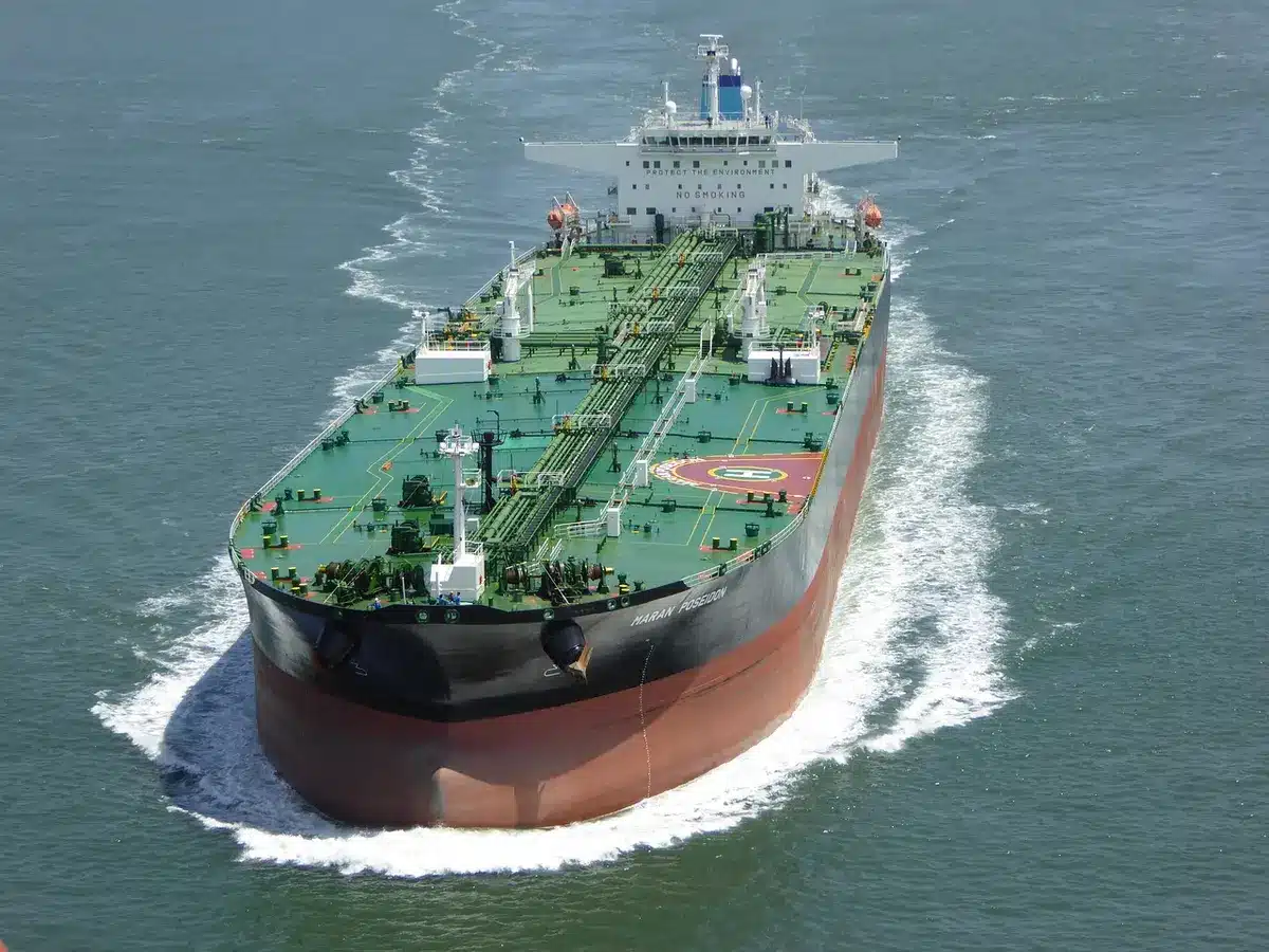 A distant, anonymous line of silhouetted tankers at sea under overcast skies, calm water, no flags or logos visible — uncertainty in oil transit