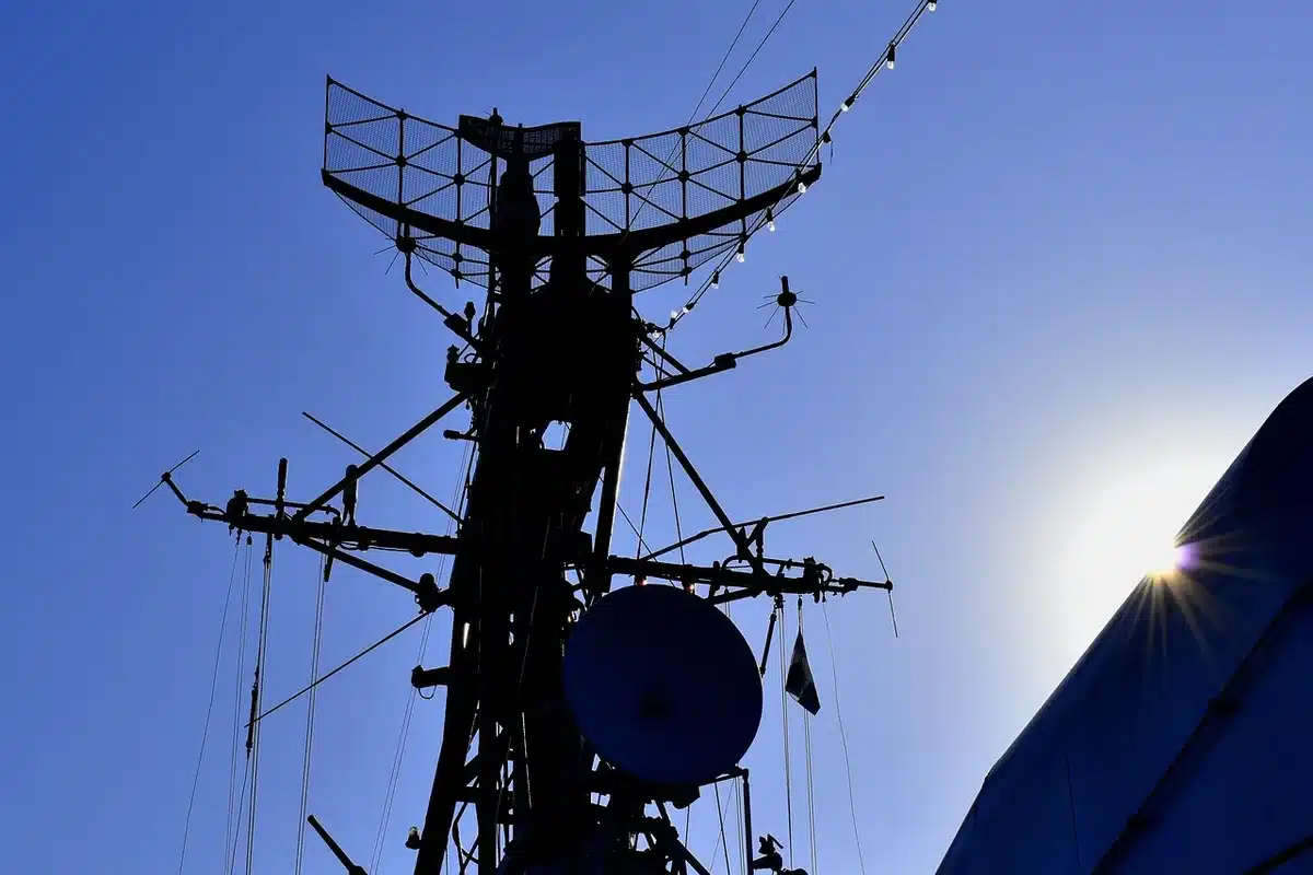 Anonymous silhouetted figure watching a bank of blank ship‑tracking radar screens in a dim operations room, fingers poised over a keyboard — concern