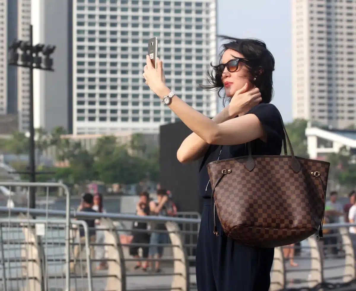A single, anonymous silhouette looking at a smartphone in soft evening light on a balcony, city skyline blurred behind — anticipation