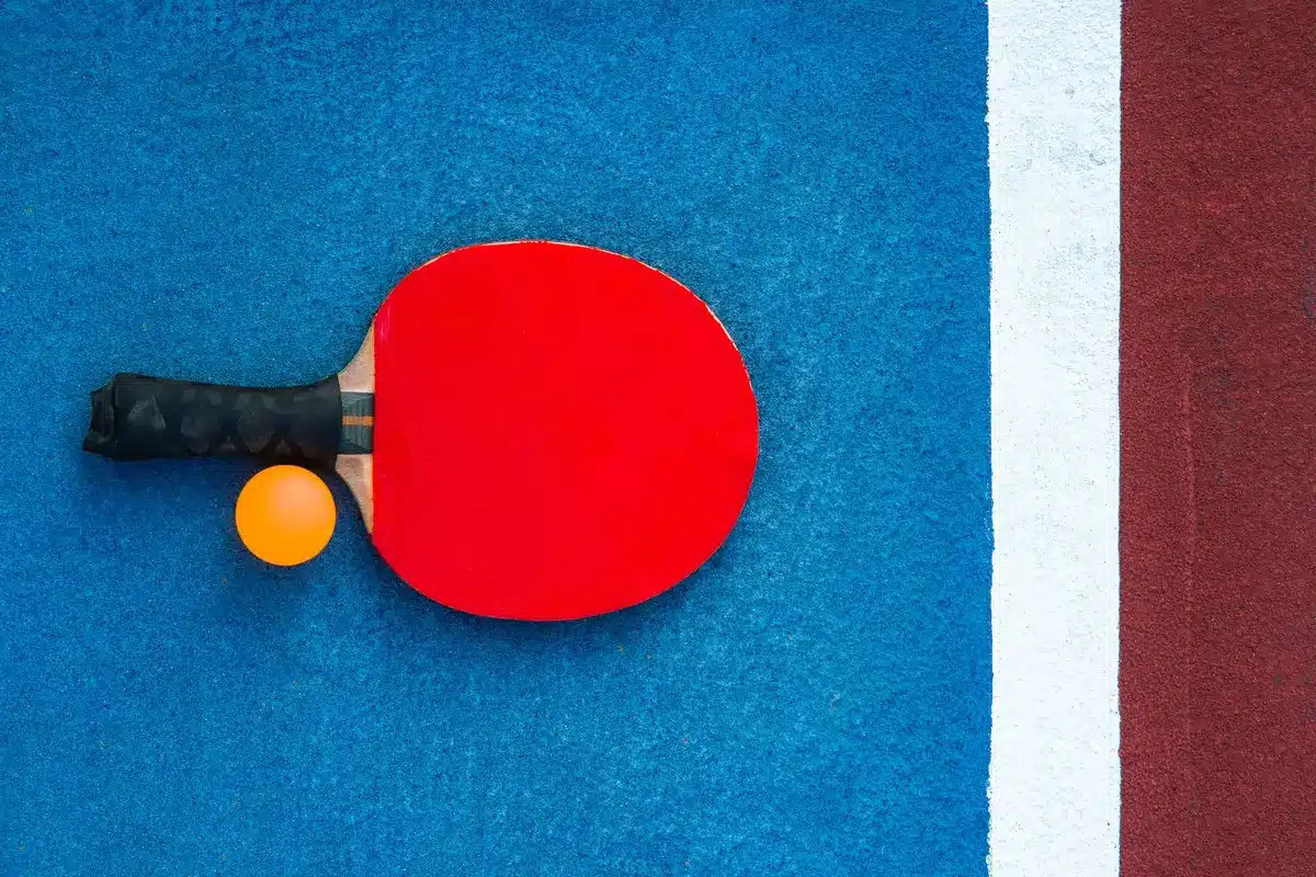 Close-up of a worn tennis racket and a single ball beside a scorer's clipboard on a bench, no logos visible