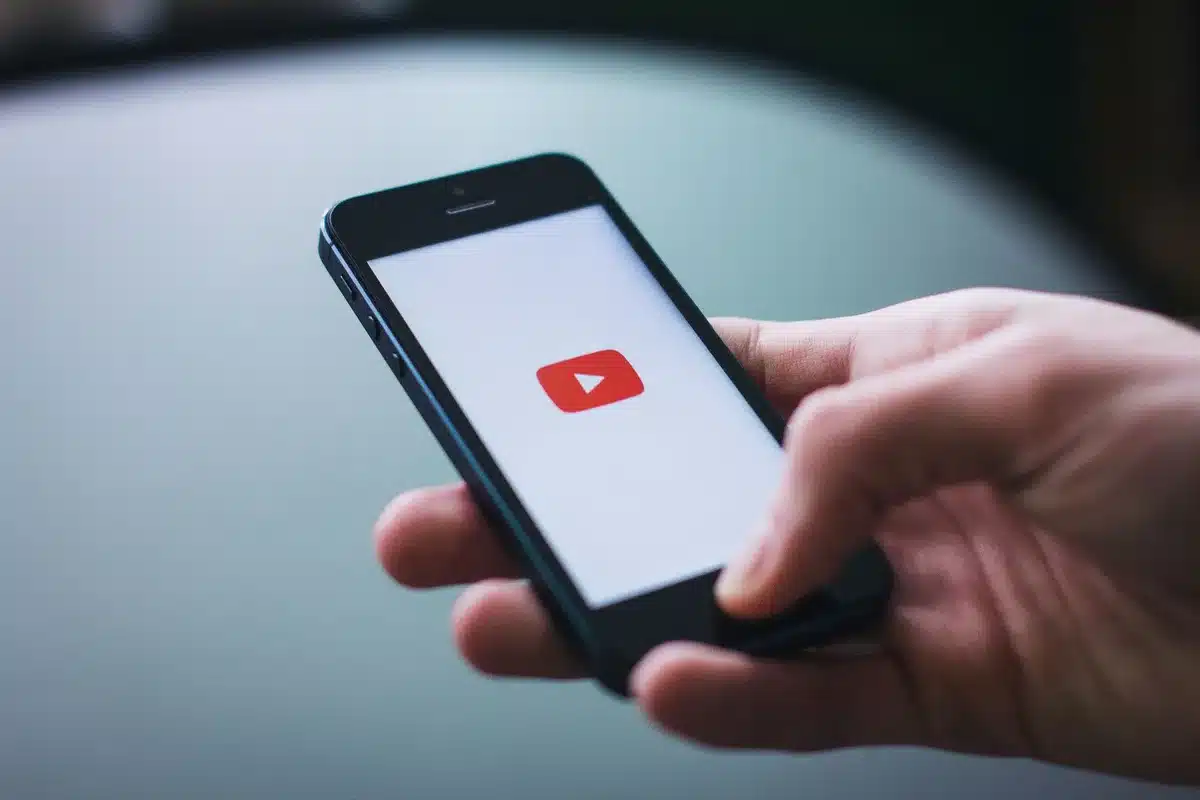 An anonymous close-up of a hand scrolling a YouTube video page on a smartphone showing a talk-show thumbnail, no faces or logos visible