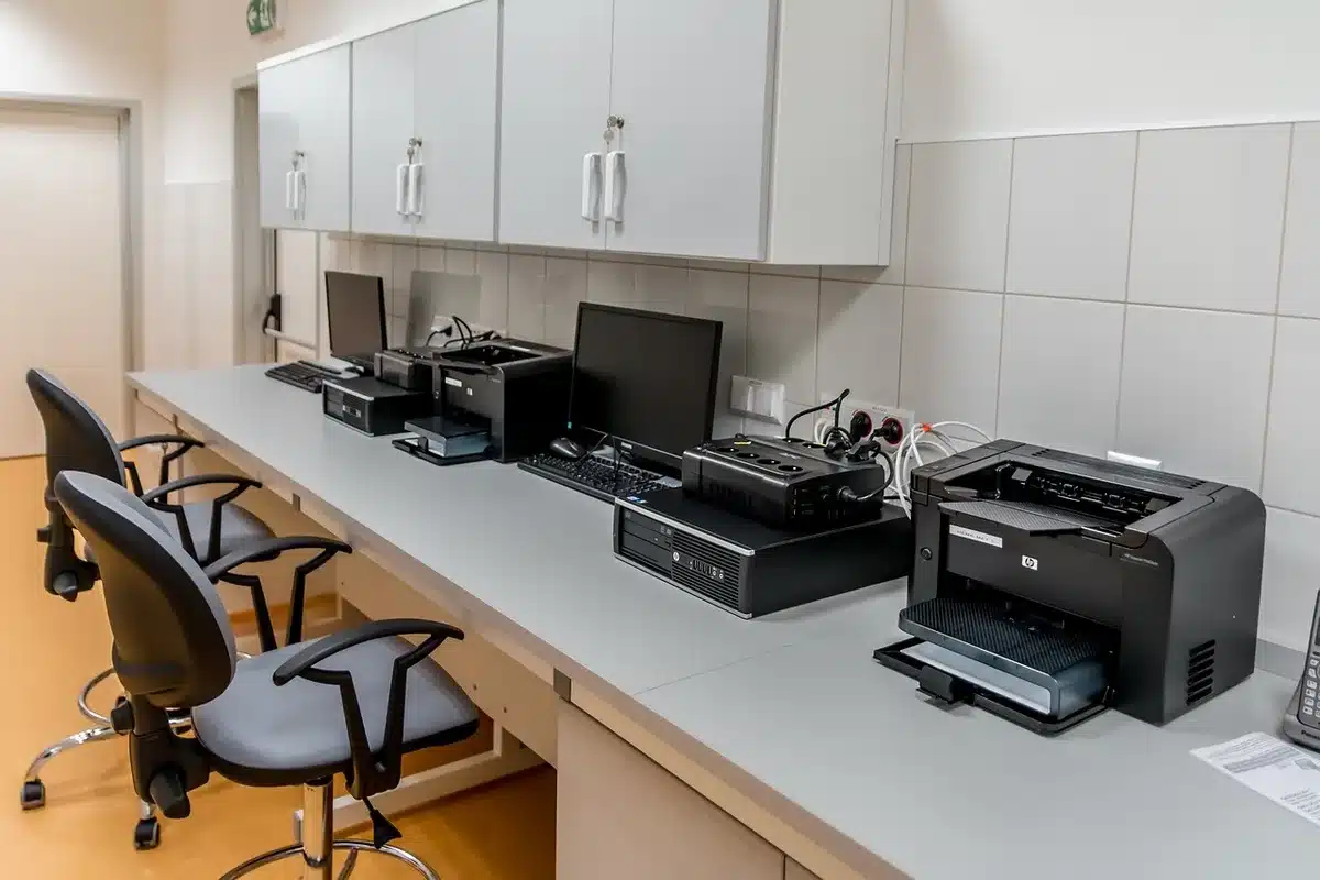 Anonymous newsroom workspace with monitors showing article lists and headlines blurred, an unbranded coffee cup at the desk, an editorial note pad nearby
