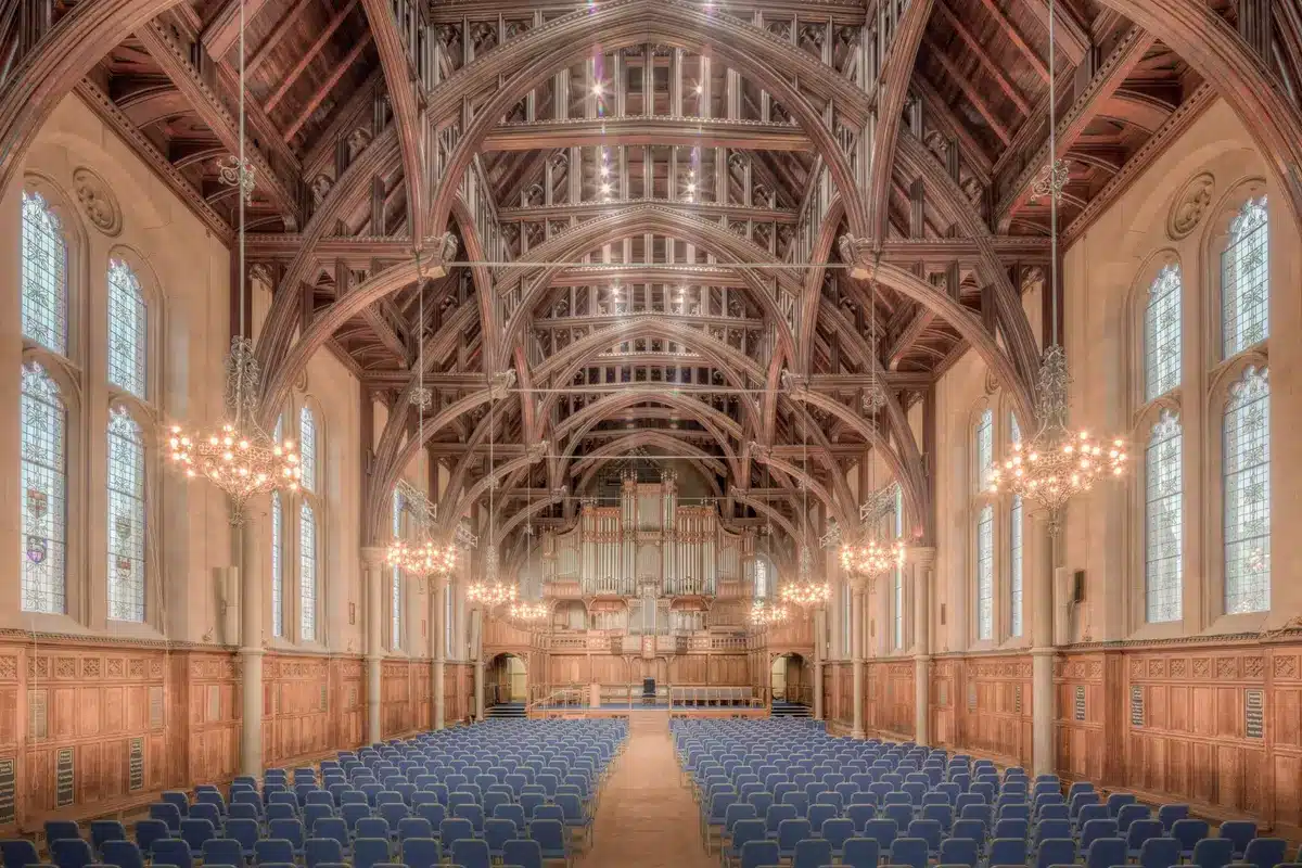 Empty conference hall with scattered chairs and a single lectern under dim lights, an anonymous envelope on the lectern suggesting a leaked recording; quiet, anticipatory scene