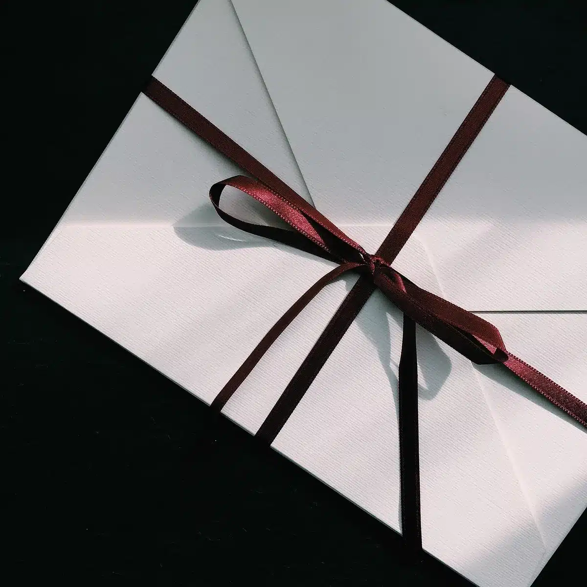 An empty formal envelope on a polished wooden desk beside a fountain pen and a folded sheet of paper suggesting a private letter