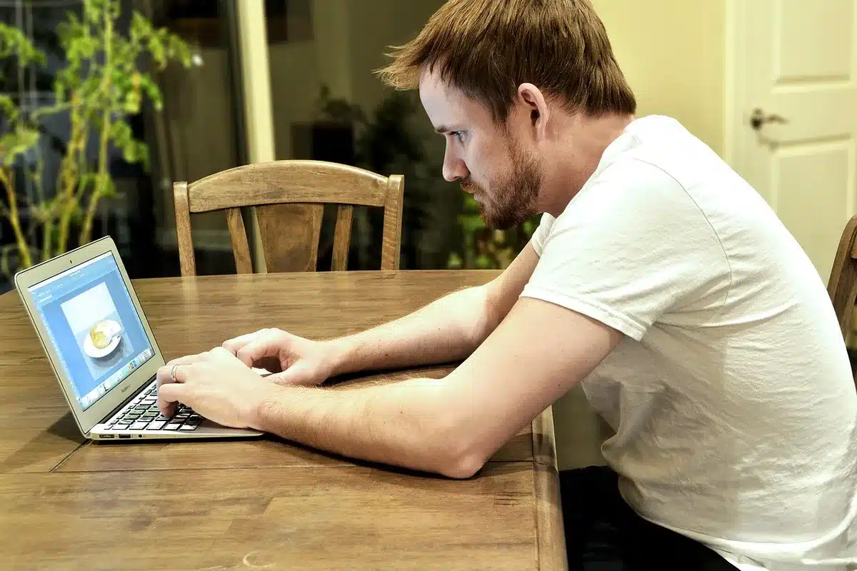 an anonymous silhouette of a person viewing a glowing news site on a laptop at a kitchen table, coffee cup nearby