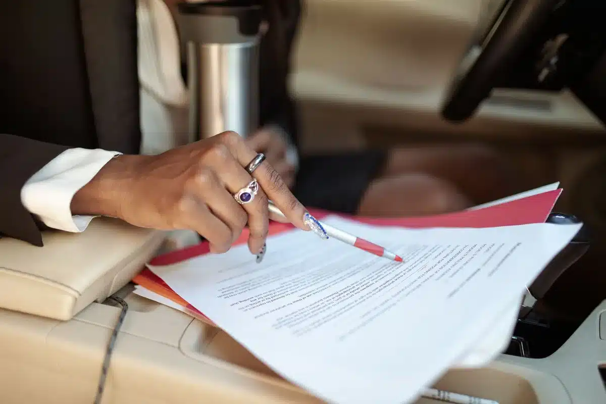 Close-up of an anonymous pair of hands resting on a legal pad next to a printed financial statement showing large rounded numbers, the digits unreadable