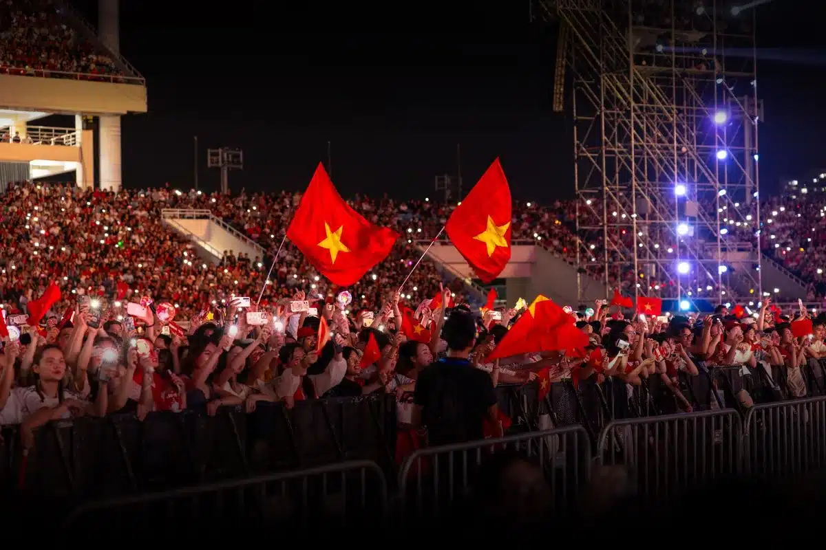 Crowd of anonymous fans under stadium lights, arms raised as confetti drifts in the air