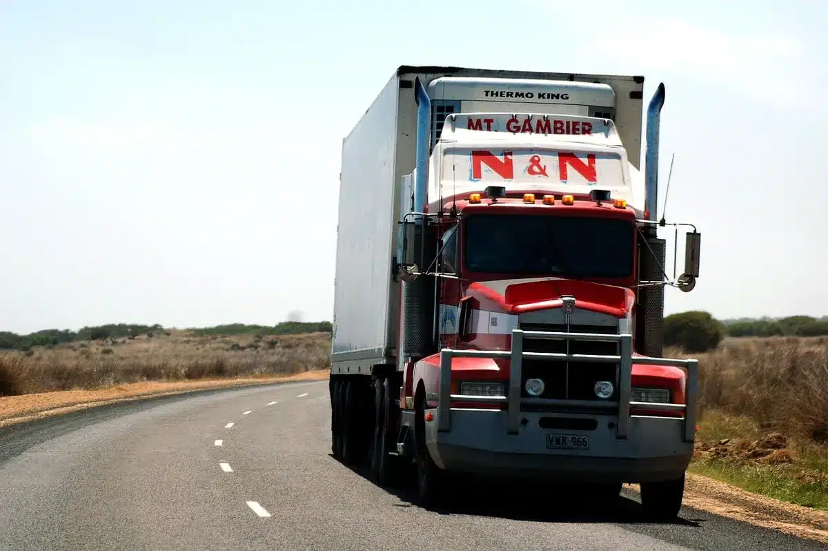 Commercial truck on highway at dawn, headlights illuminating the road ahead