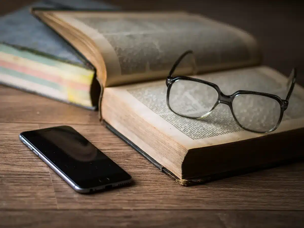 an anonymous paperback book and reading glasses on a side table next to a closed notepad, a cup of tea with a faint steam wisp visible
