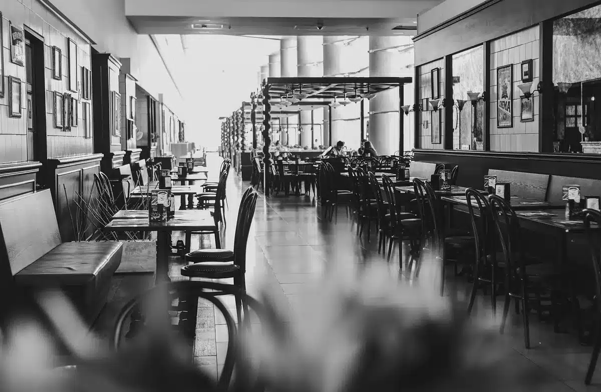 An empty restaurant dining room with stacked chairs and a dimmed register, an unbranded counter and menu board blurred in the background suggesting a corporate dining chain undergoing change