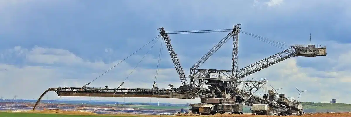 A wide shot of a new open-pit mining site at dawn, heavy earthmoving equipment on the bench and a distant pile of crushed rock, no people visible