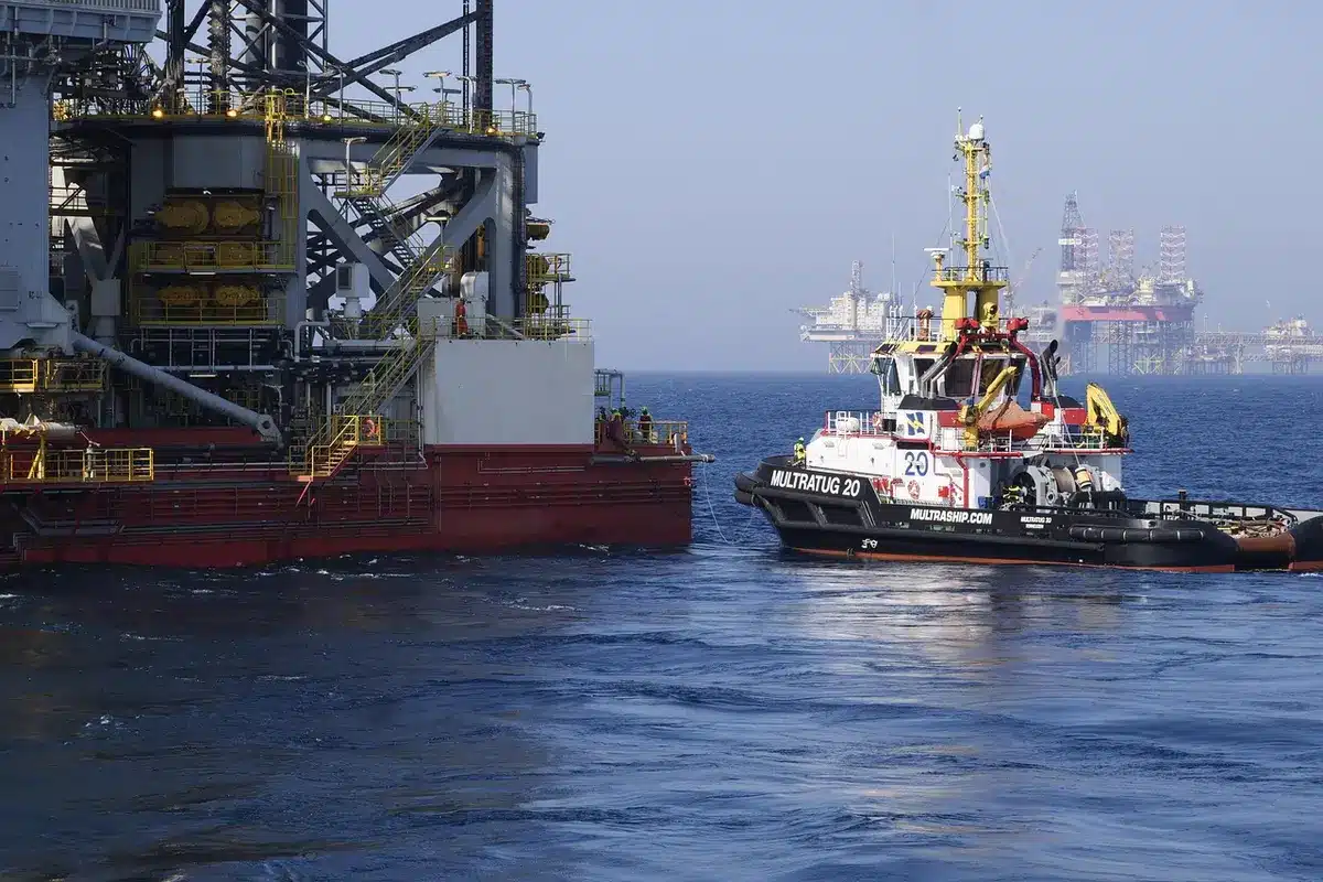 Offshore oil platform under construction in the South Atlantic, industrial structures rising above blue-grey waters, heavy equipment and cranes visible, stormy skies overhead