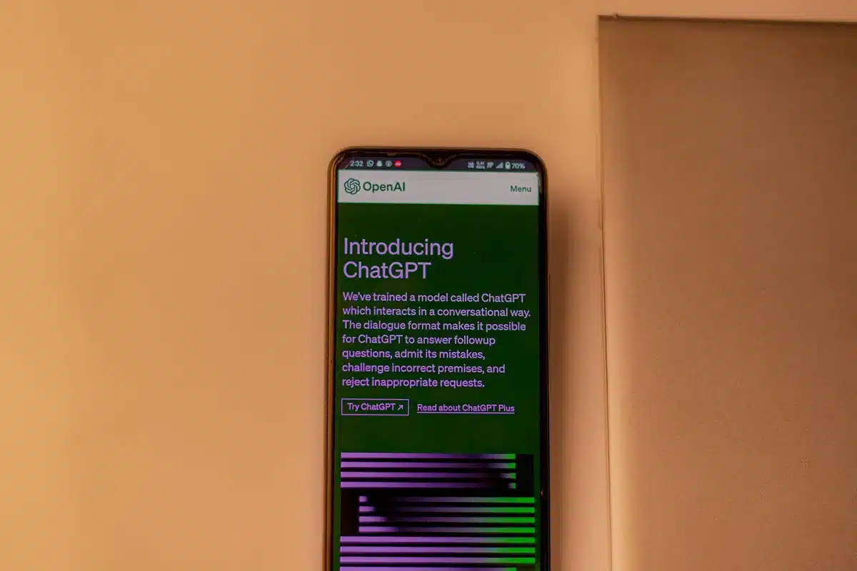 A dimly lit smartphone on a plain table displaying an unbranded assistant interface, the screen glow reflected on the surface, an anonymous hand reaching in from the side as if about to tap; anticipation in the shot