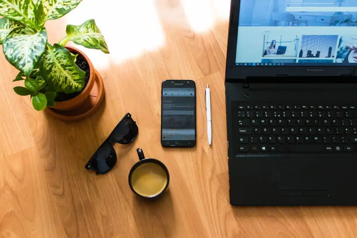 A sleek smartphone on a simple wooden desk showing a generic messaging interface placeholder, a cup of coffee and a notepad beside it