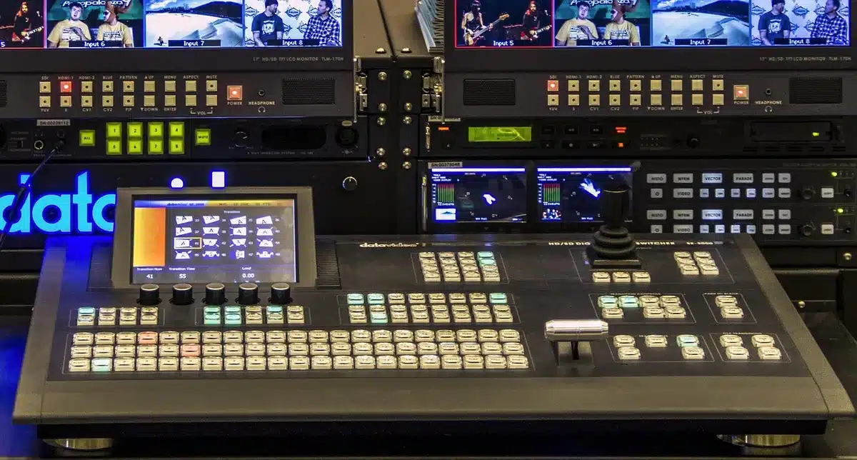An empty television studio desk with two anonymous chairs and a stacked pile of loose policy briefing papers on the table, a blank broadcast monitor in the background suggesting a live cable-news set