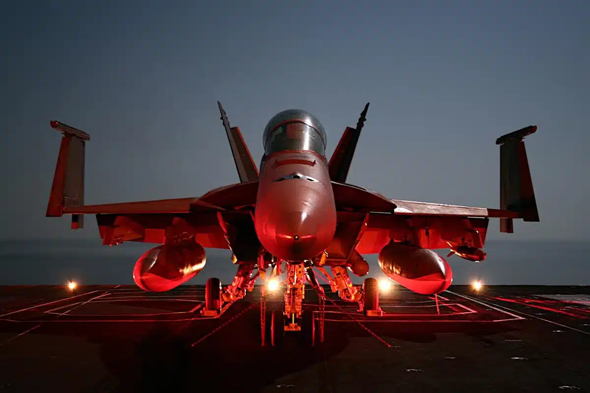 An empty carrier flight deck at dawn with a single unbranded prototype jet model on the catapult, deck crew silhouettes distant and blurred