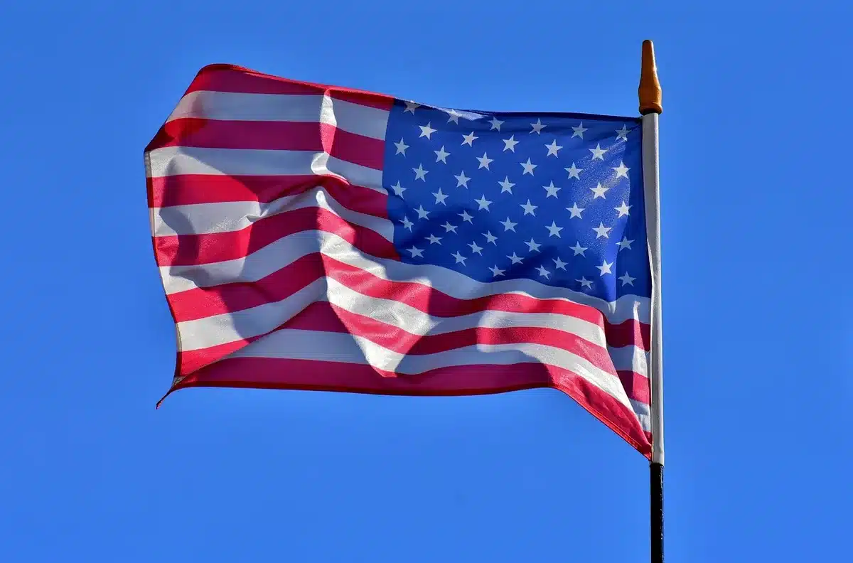 A dim flagpole against an overcast morning sky, a single unbranded flag lowered to half-staff, empty municipal steps below