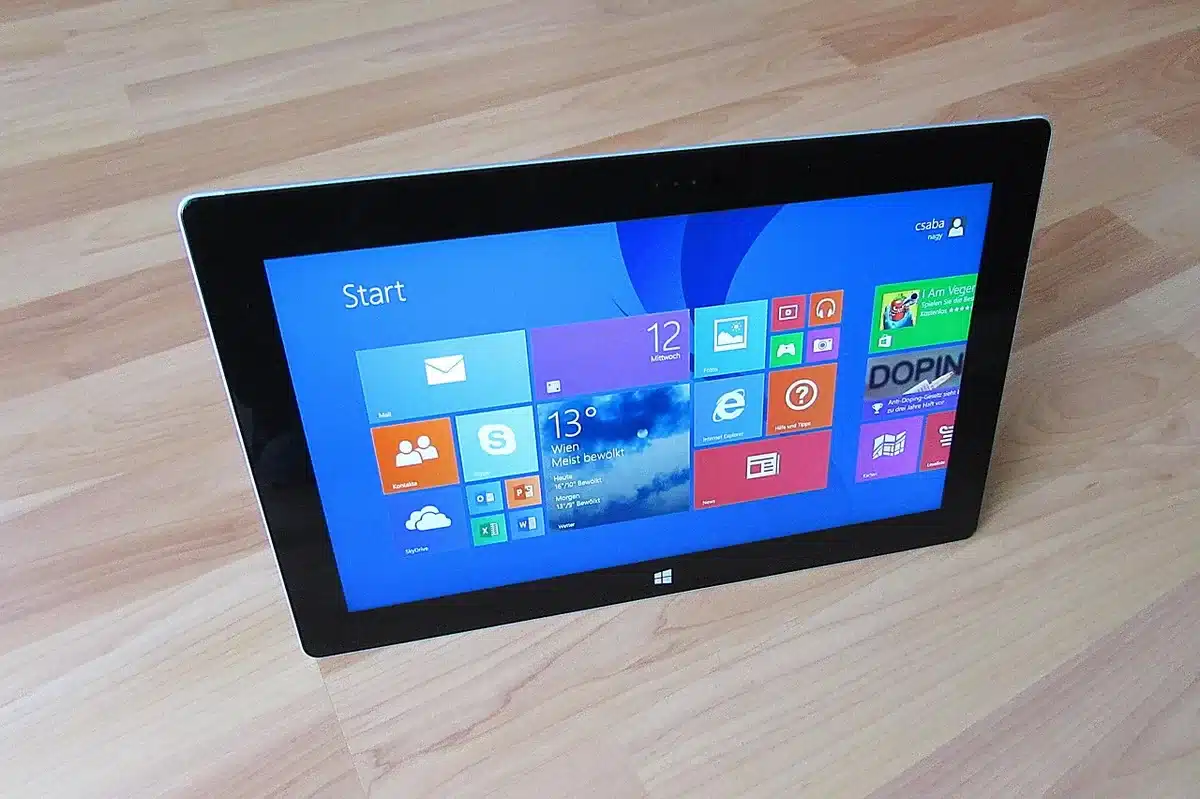 a symbolic close-up of an anonymous hand scrolling a tablet that displays blurred headline tiles, the tablet on a plain wooden table, no brand visible