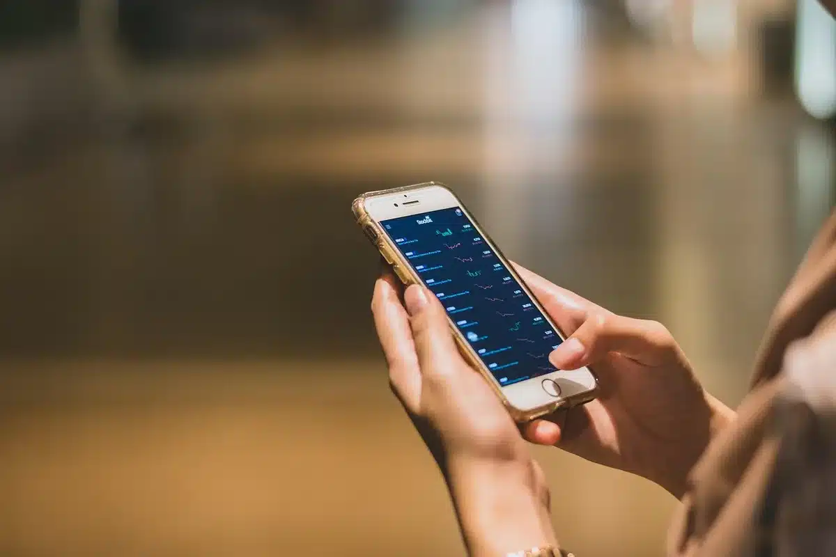 Close view of an anonymous pair of hands holding a smartphone showing a blank sports app interface, a blurred stadium in the background, no branding visible