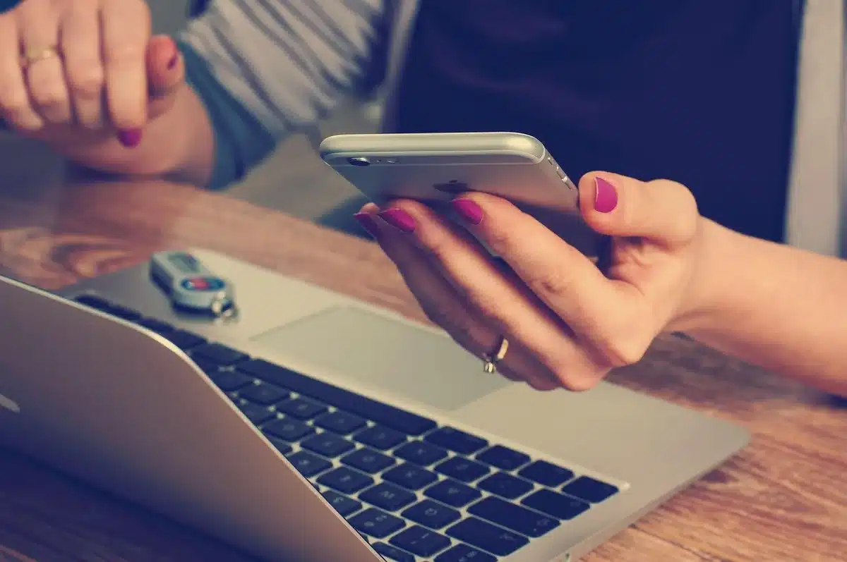 An anonymous pair of hands holding a smartphone showing a blank benefits app screen, a pile of mailed bills on a table nearby — tension