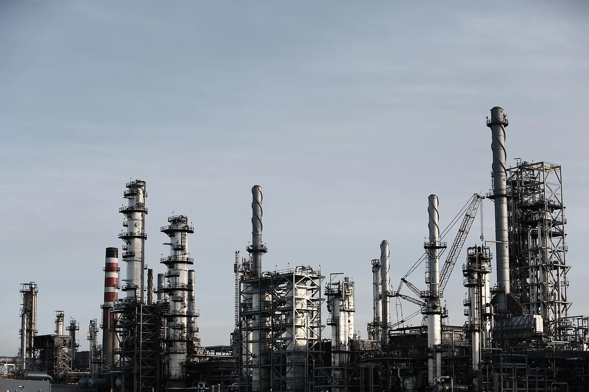 A modern manufacturing floor with industrial machinery and equipment, workers in safety gear moving through the space, metal components on assembly lines, bright overhead lighting casting sharp shadows, sense of productivity and precision