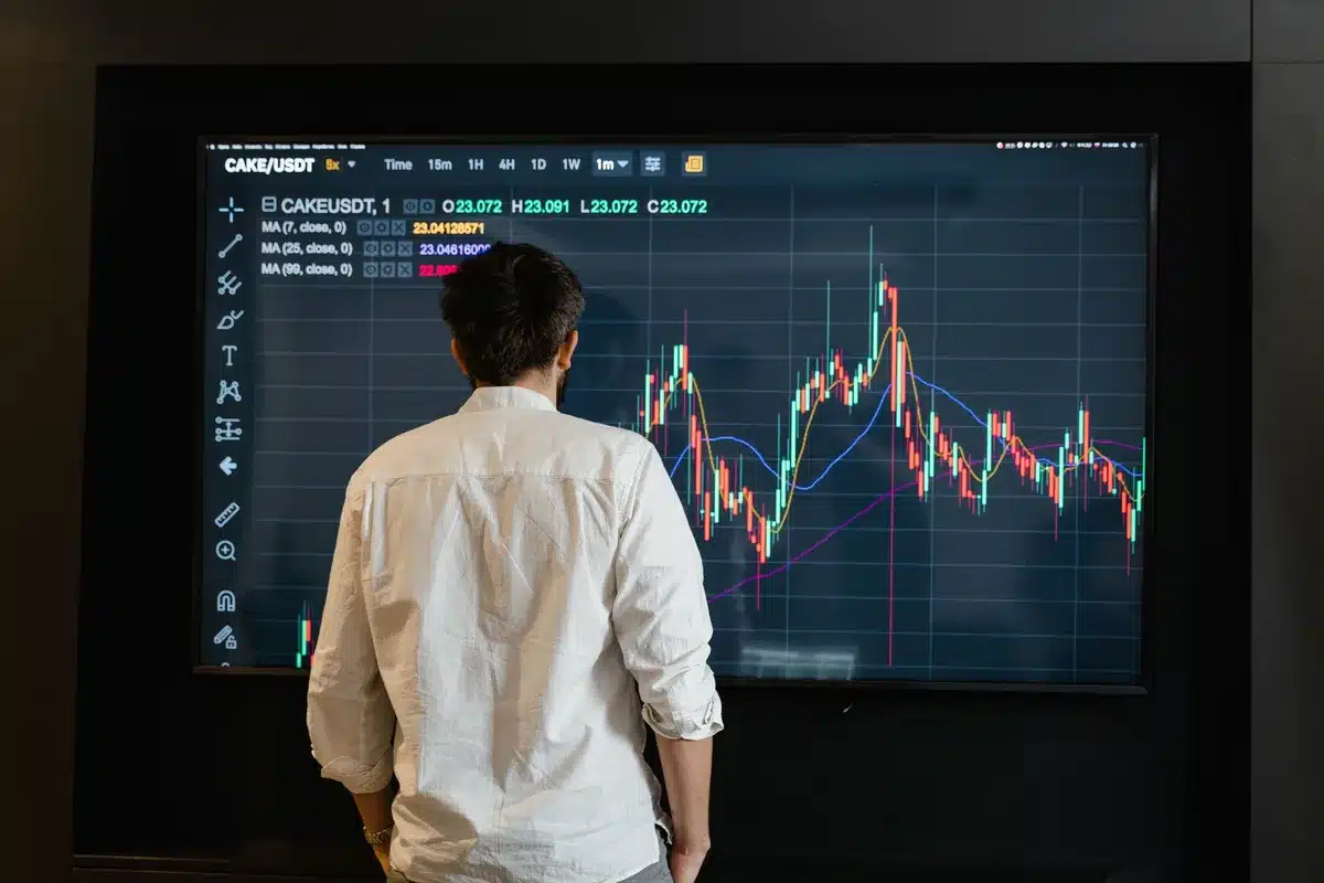 Close-up of a generic laptop displaying candlestick charts and a rising price line, with an anonymous hand nearby