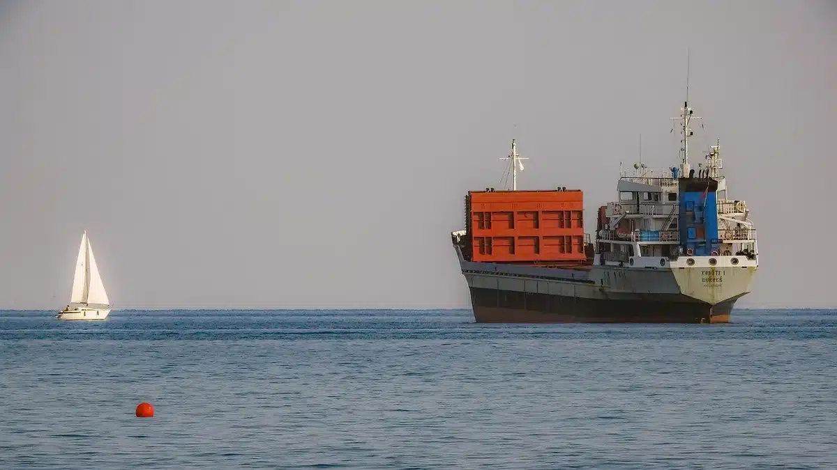 Anonymous silhouette of a cargo tanker at sea under overcast skies, distant cranes and a low horizon line
