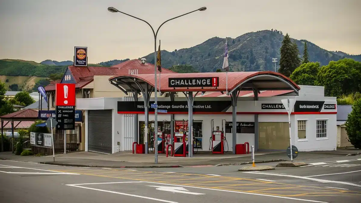A dim, anonymous fuel station forecourt at dusk with empty pumps and a distant highway, suggesting higher fuel costs